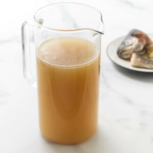 Pitcher of homemade fish broth. Saucer in the background with fish head and tail.