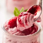 A spoon in a dish of raspberry mouse cake filling.