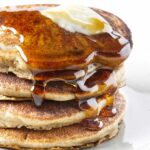 A stack of sprouted wheat pancakes with syrup and butter on top.