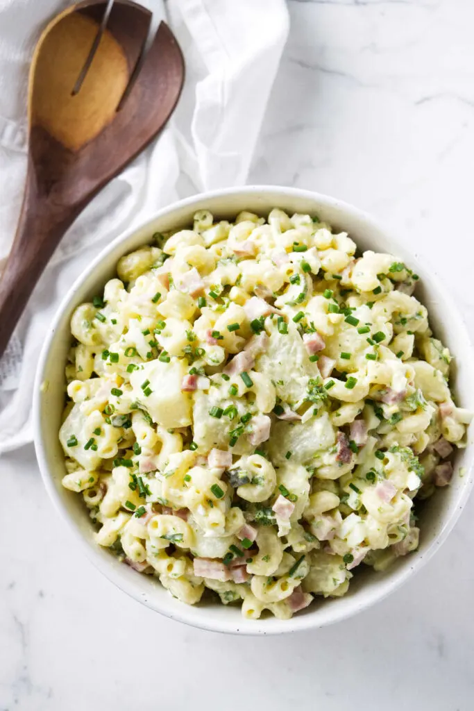 A bowl filled with Hawaiian potato macaroni salad next to a wooden spoon.