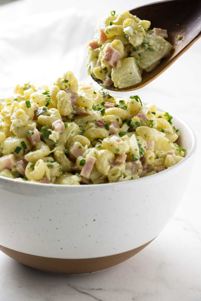 A spoon scooping some potato mac salad from a bowl.