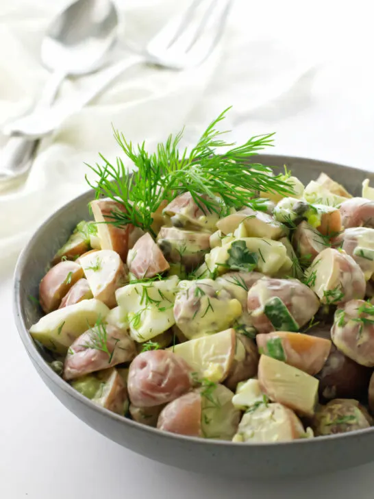 A serving bowl filled with baby red potato salad with creamy yogurt dressing.