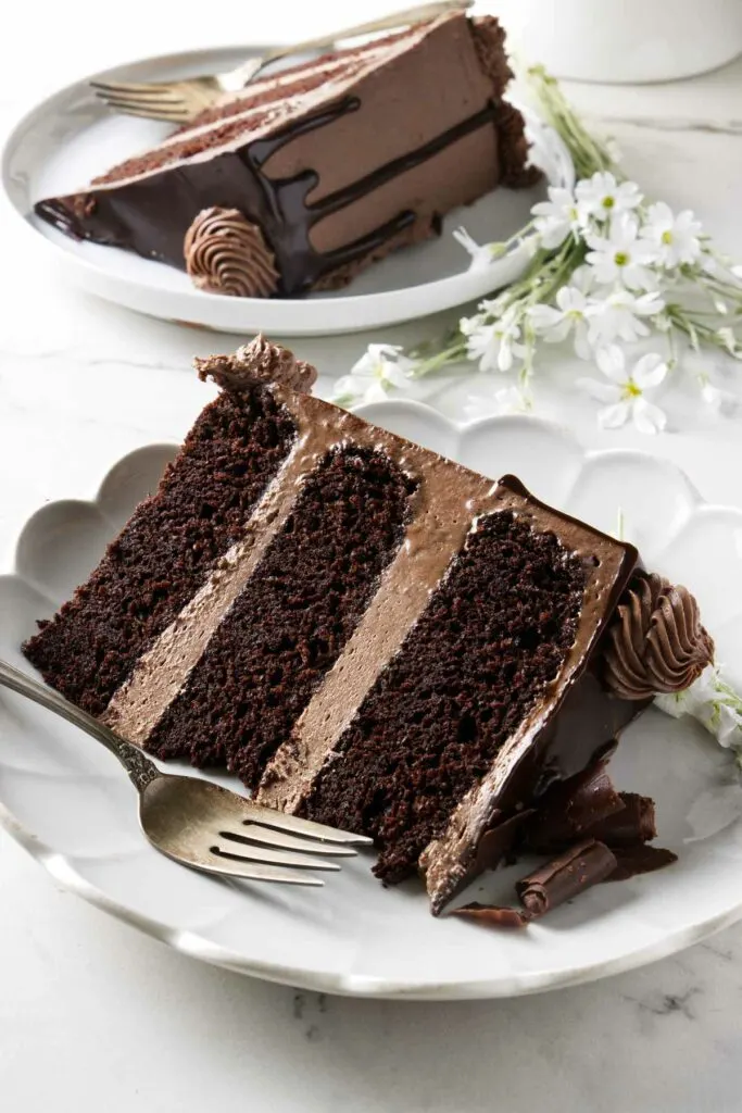 Two slices of triple chocolate cake on white plates.