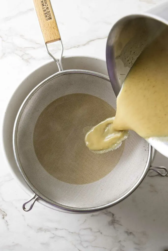 Straining butter ice cream custard through a metal strainer.