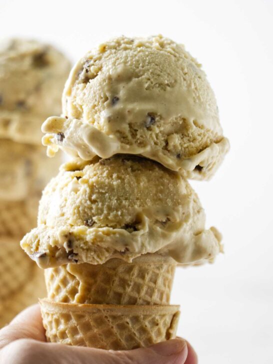 Two scoops of brown butter ice cream with toffee bits on a sugar cone.