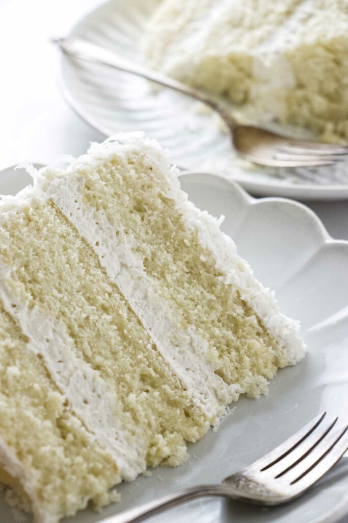 Two slices of coconut buttercream cake on plates.