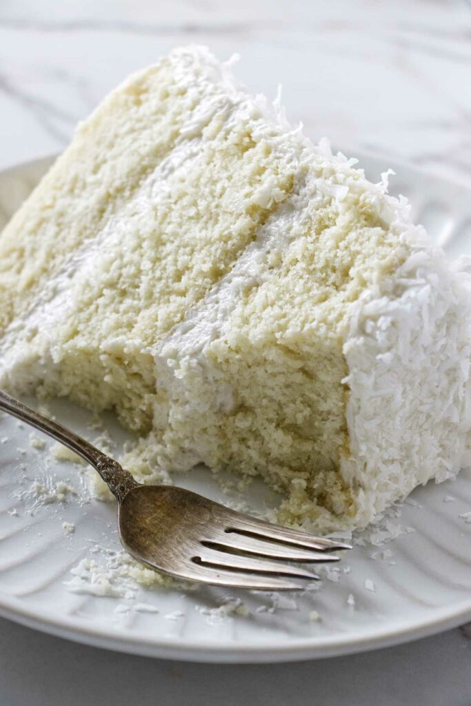 A partially eaten slice of coconut cake with coconut buttercream frosting.