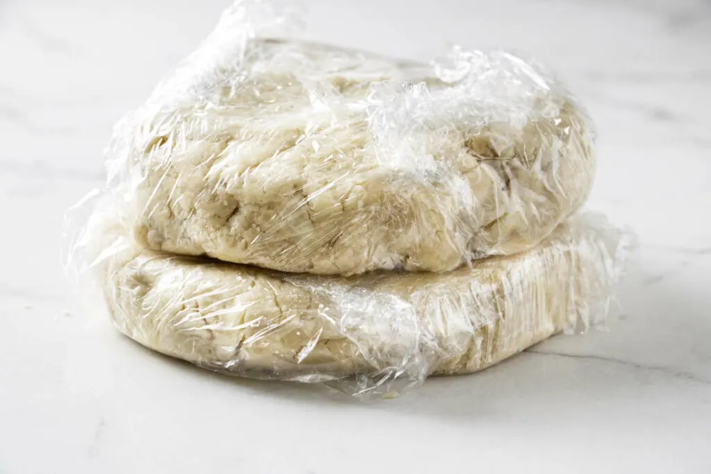 Two disks of pie dough wrapped in plastic wrap.