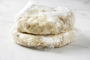Two disks of pie dough wrapped in plastic wrap.