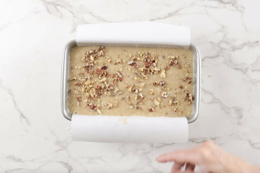 Adding banana bread batter to a loaf pan.