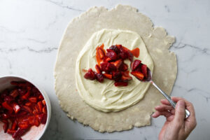 Spooning strawberries on top of a cream cheese mixture.