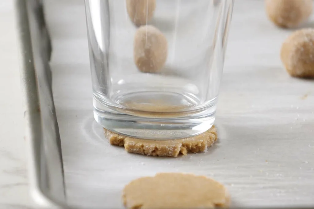 Flattening a ball of cookie dough with a glass.