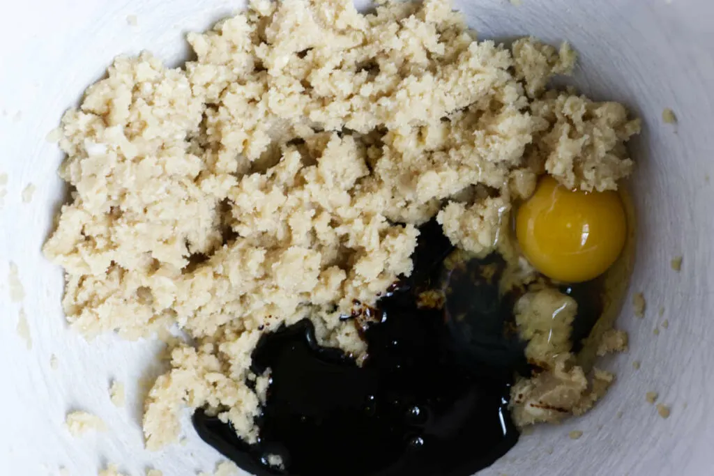 Molasses and an egg in a mixing bowl with creamed butter and sugar.