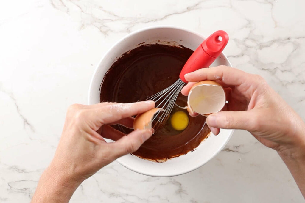 Adding and egg to chocolate cake batter.