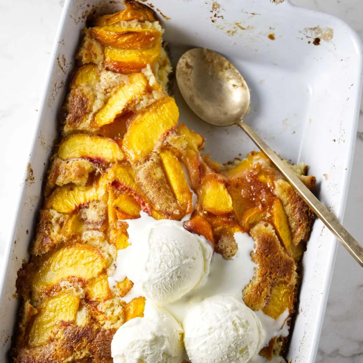 A partially eaten peach coffee cake with vanilla ice cream on top.