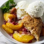 Raspberry peach cobbler with buttermilk biscuits in a bowl with ice cream.