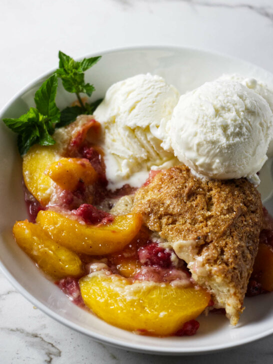 A serving of raspberry peach cobbler in a bowl with ice cream.