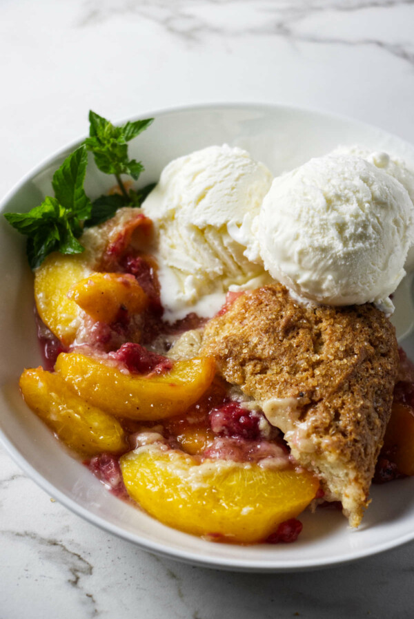 A serving of raspberry peach cobbler in a bowl with ice cream.