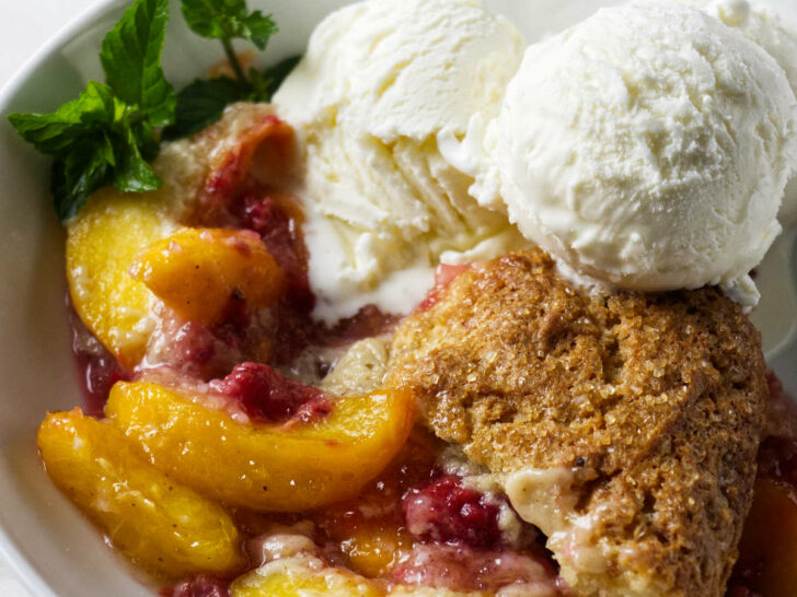 A serving of raspberry peach cobbler in a bowl with ice cream.