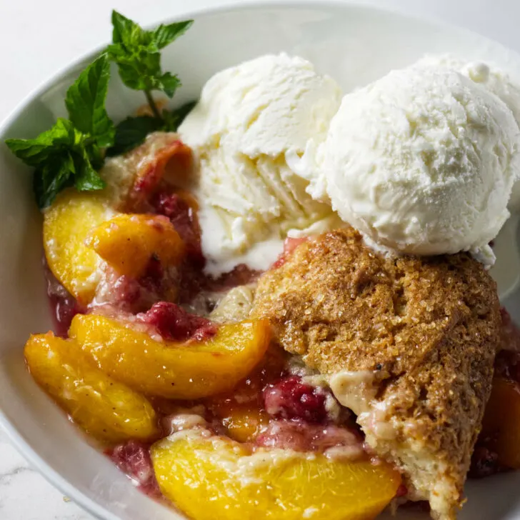 A serving of raspberry peach cobbler in a bowl with ice cream.