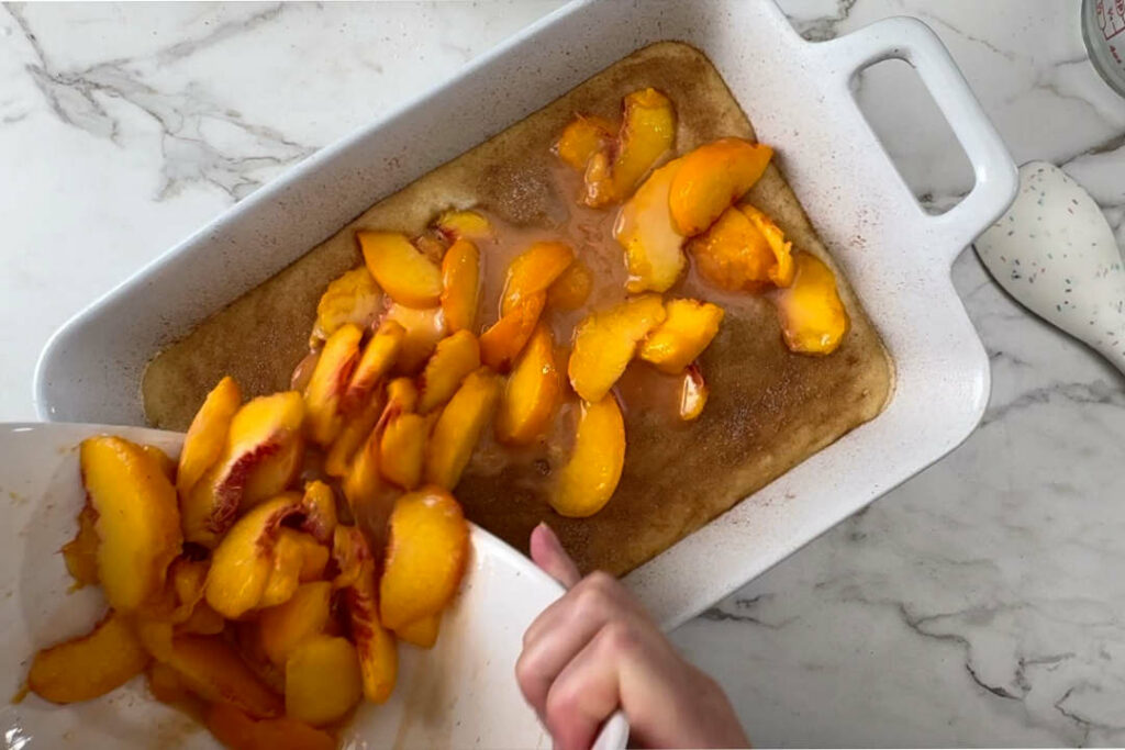 Pouring sliced peaches on top of coffee cake batter.