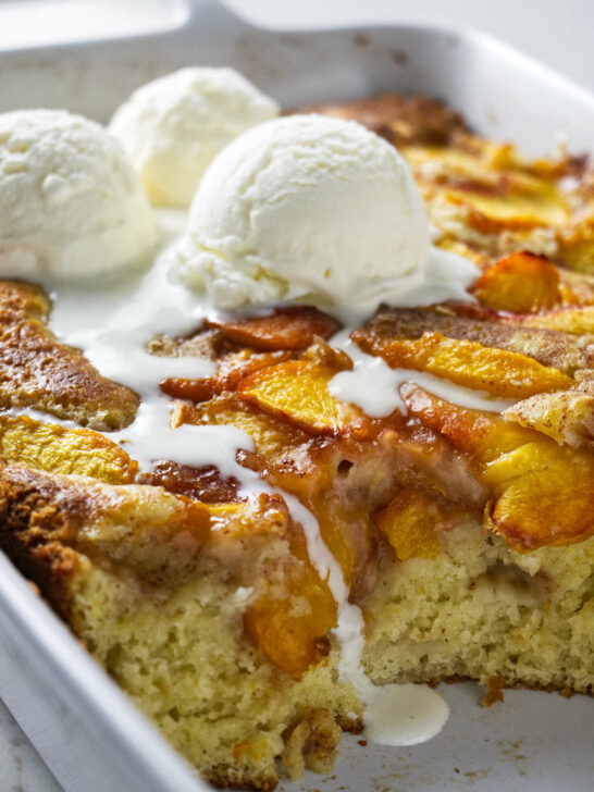 A peach coffee cake in a baking dish with 3 scoops of ice cream on top.