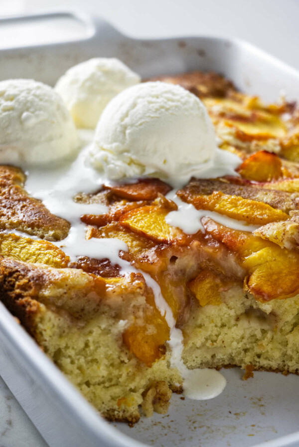 A peach coffee cake in a baking dish with 3 scoops of ice cream on top.