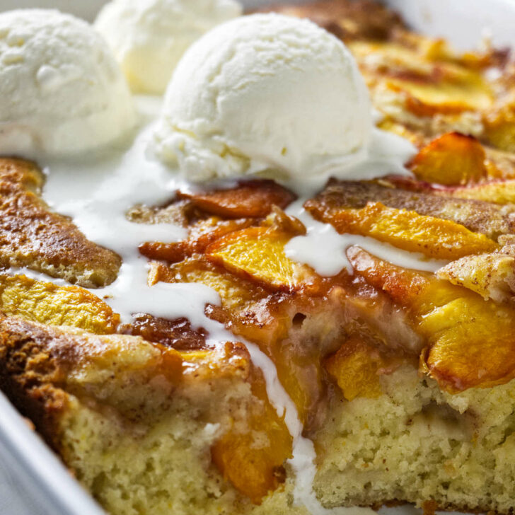 A peach coffee cake in a baking dish with 3 scoops of ice cream on top.