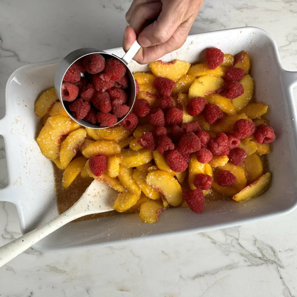 Mixing the peaches and raspberries in a baking dish.