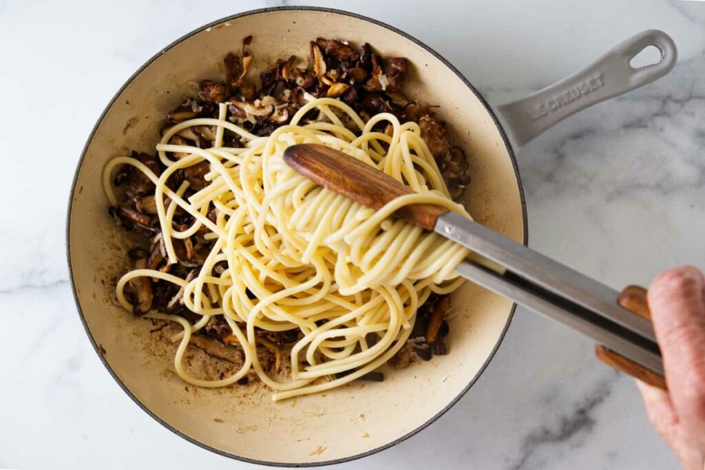 Adding pasta to a skillet with wild mushrooms.