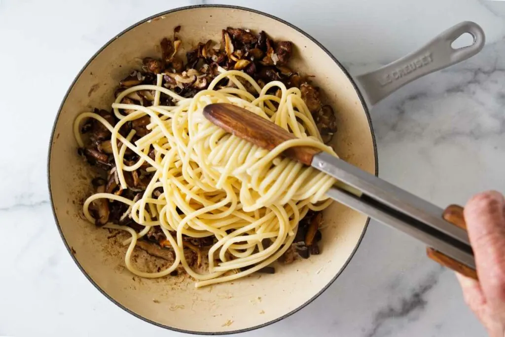 Adding pasta to a skillet with wild mushrooms.