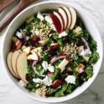 A massaged kale salad with cranberries and apples in a bowl.