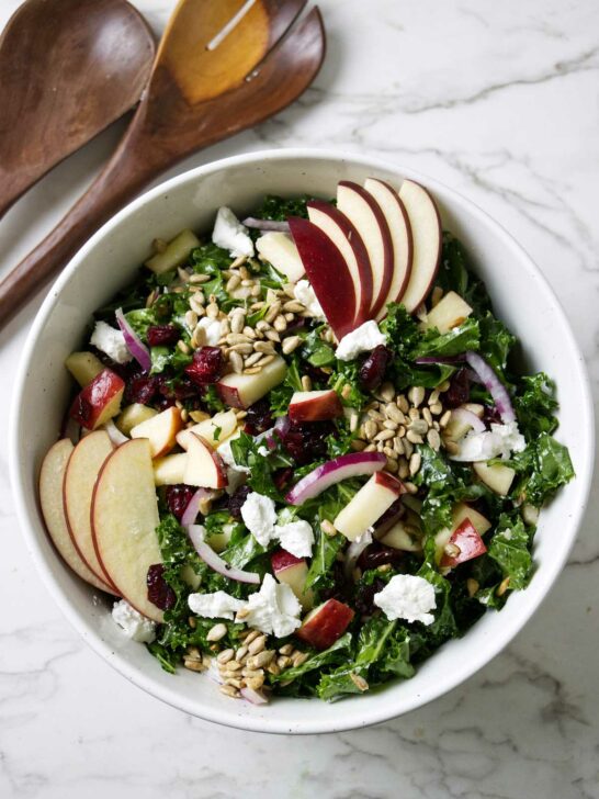 A kale salad with cranberries and apples in a large bowl.