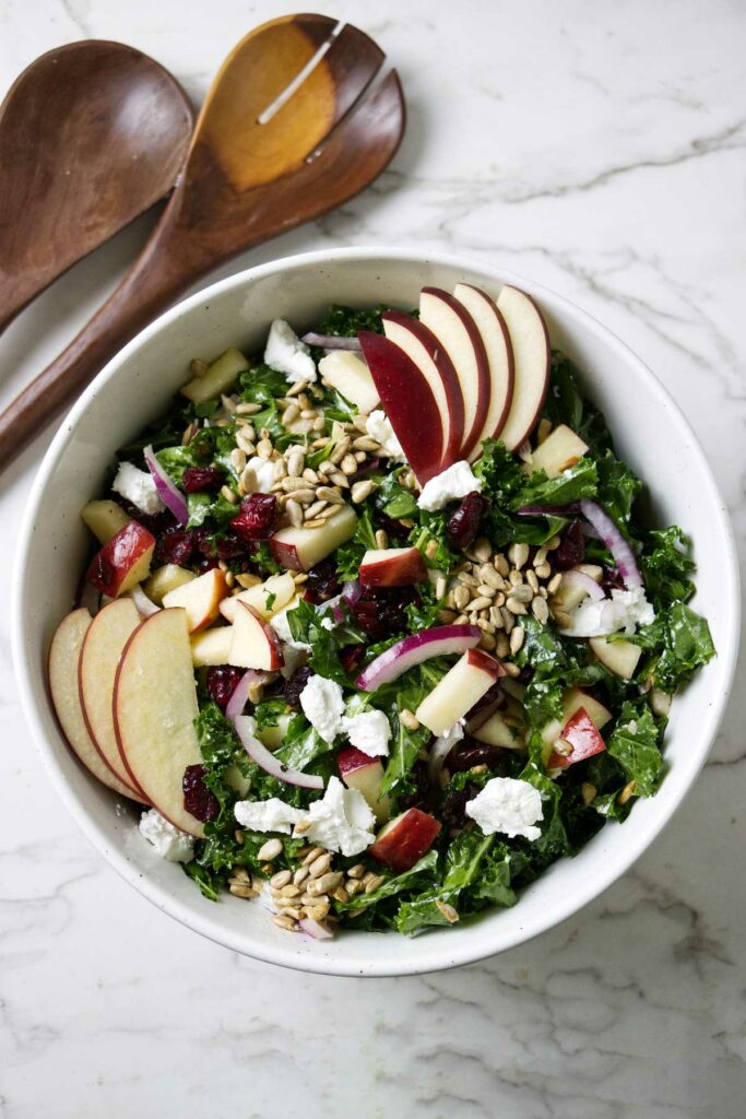 A kale salad with cranberries and apples in a large bowl.