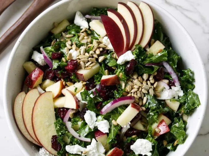 A kale salad with cranberries and apples in a large bowl.