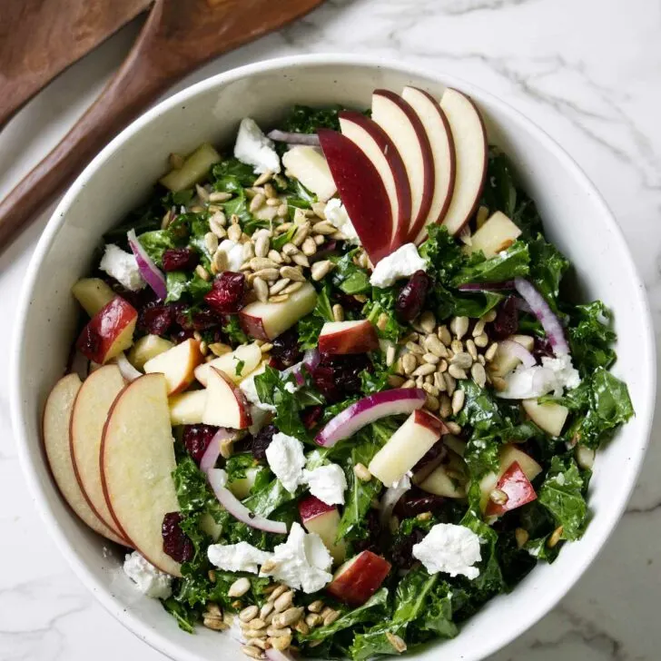 A kale salad with cranberries and apples in a large bowl.