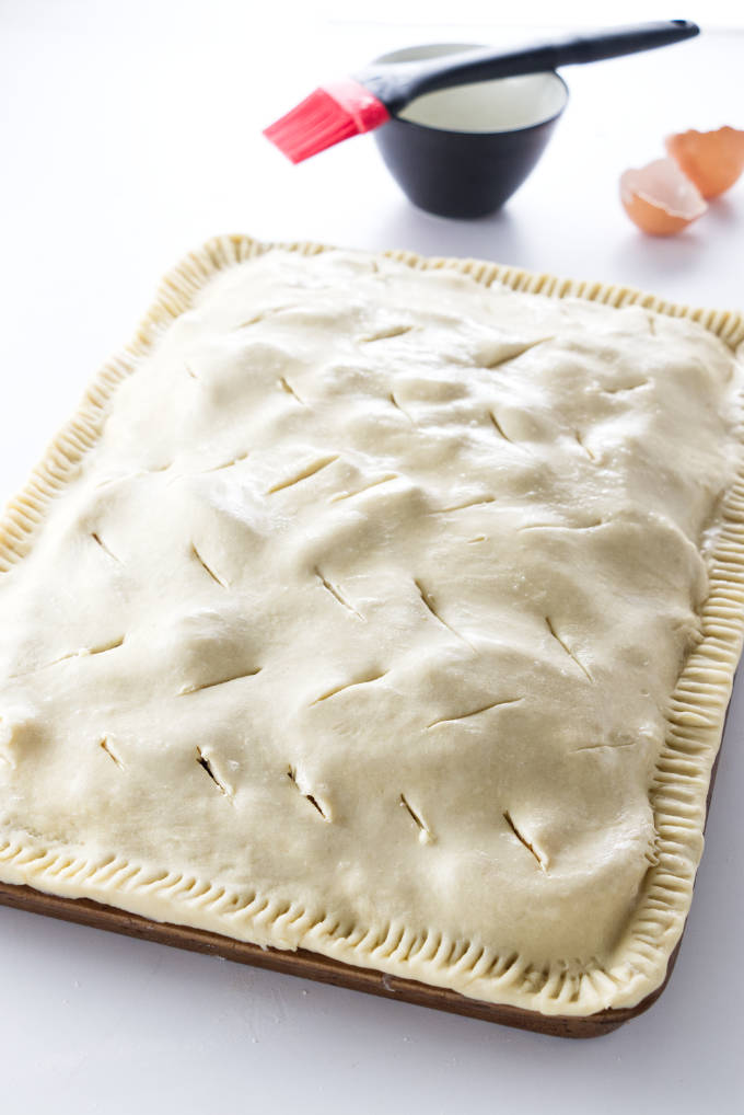 Adding the top crust to a apple slab pie recipe.