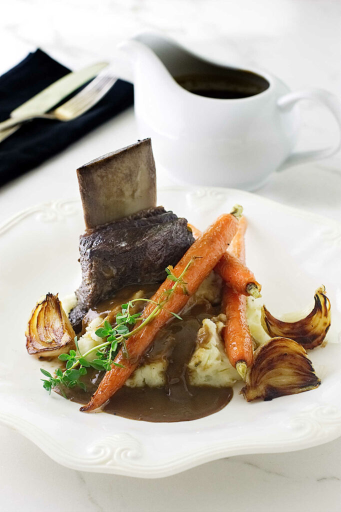 Beer braised beef short ribs on a plate with gravy in the background.