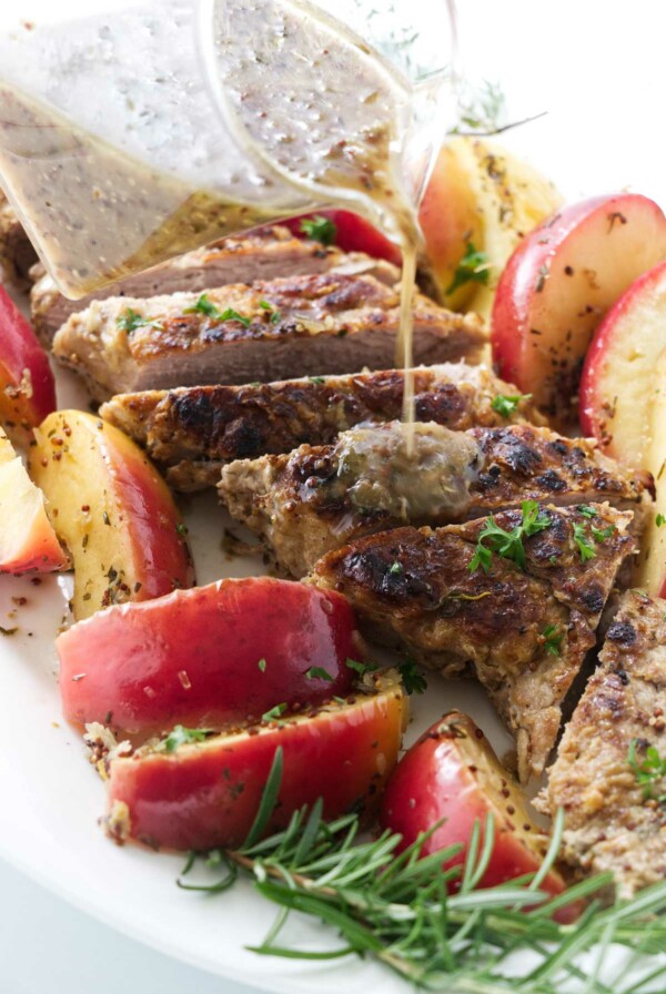 Pouring sauce over a cider braised pork tenderloin with baked apples.