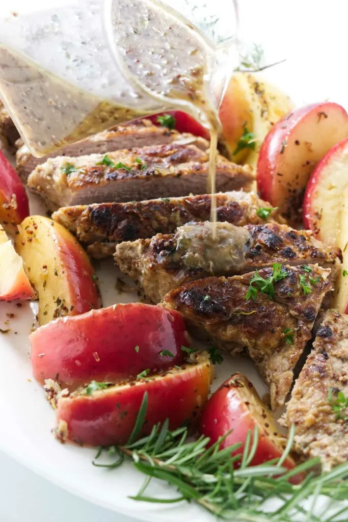 Pouring sauce over a cider braised pork tenderloin with baked apples.