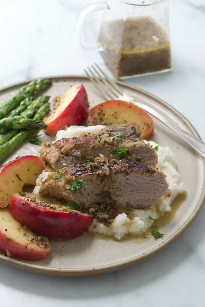 Apple cider braised pork tenderloin on a plate with apples and potatoes.