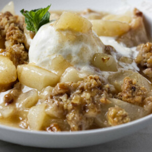 A pear crisp with fresh pears and a scoop of ice cream.