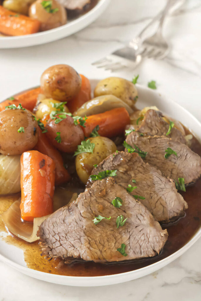 Slices of tri tip instant pot on a plate with carrots and potatoes.