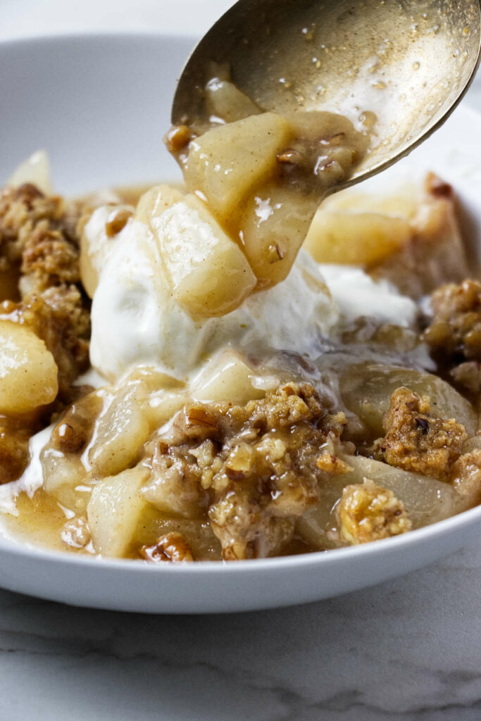 Spooning an old fashioned pear crisp recipe over ice cream.