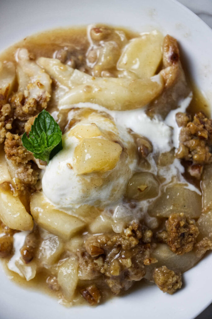 Fresh pear crisp in a bowl with ice cream.