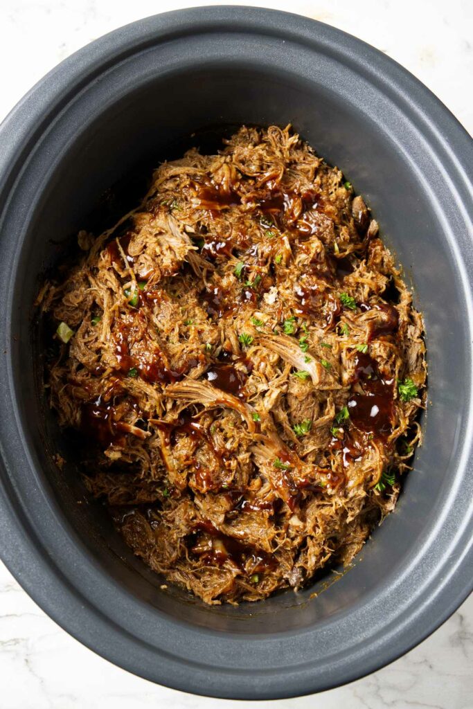 Slow cooker shredded pork in a crockpot with bbq sauce.