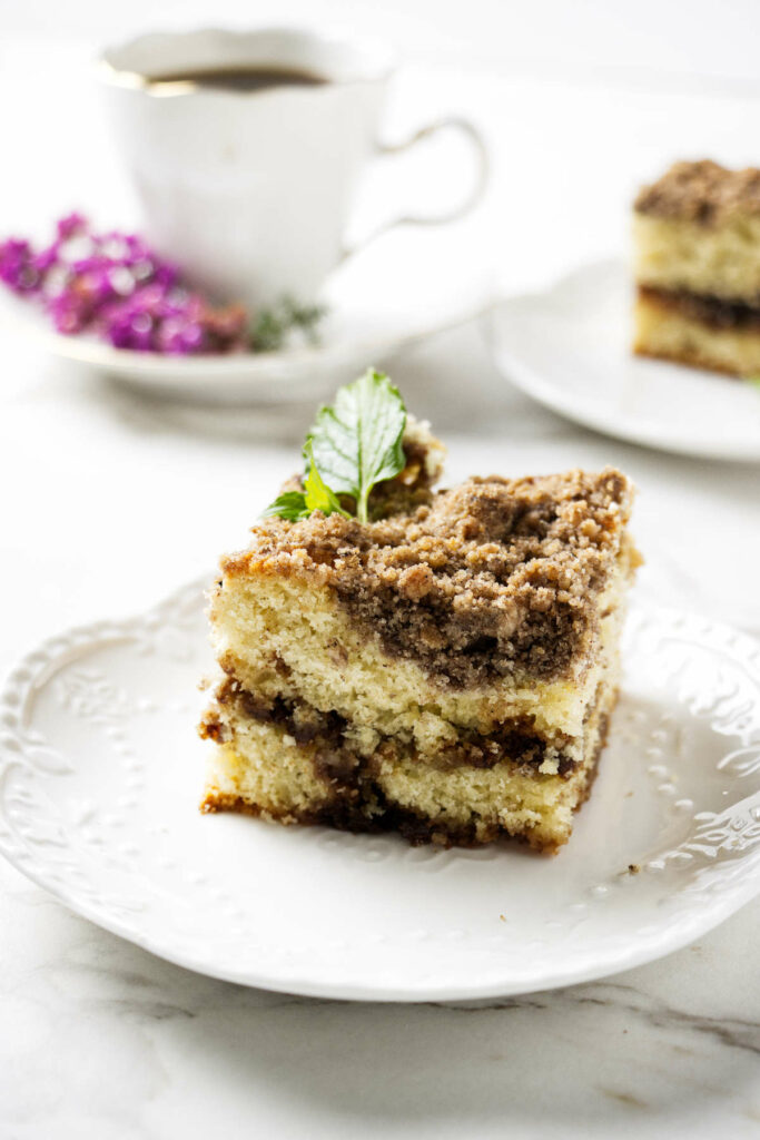 A slice of sourdough coffee cake on a plate with coffee in the background.