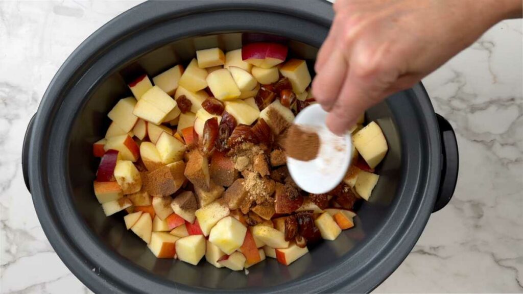 Adding spices and dates to a crockpot to make sugar free apple butter.