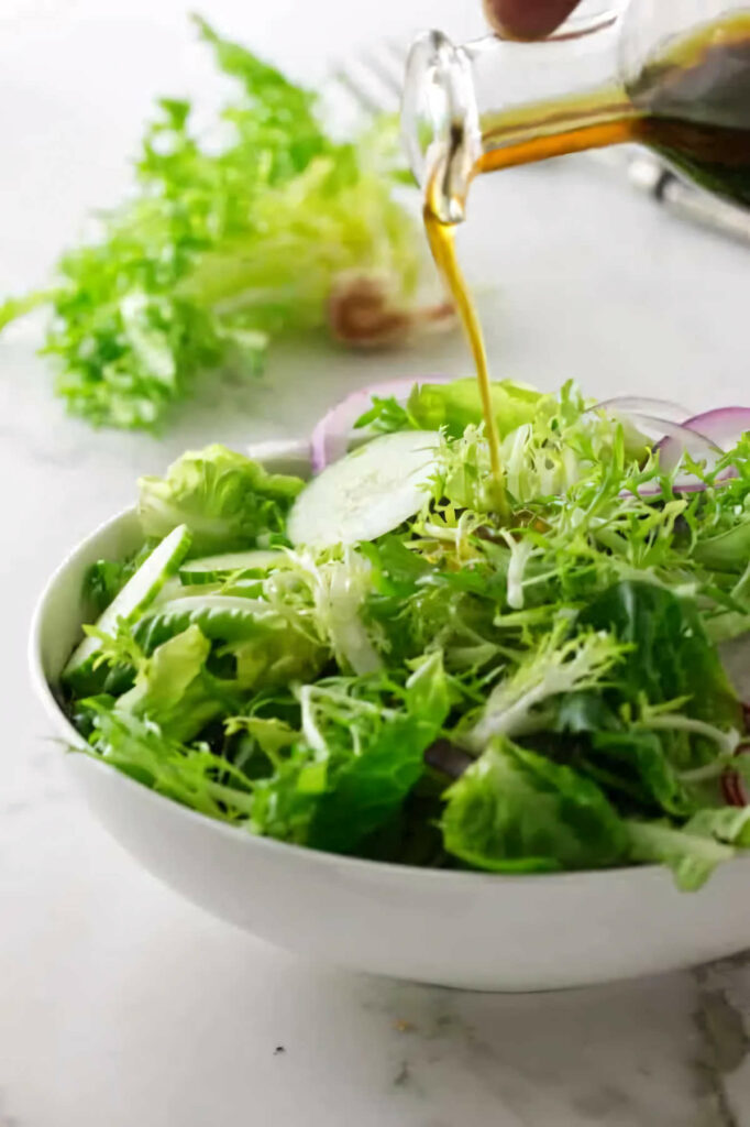 Pouring vinaigrette on salad greens.