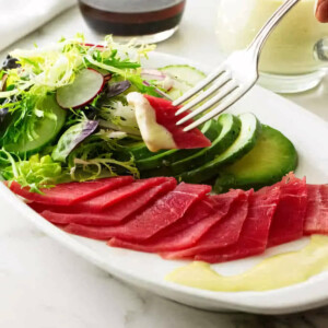 A fork holding a bite of a tuna sashimi salad with wasabi dressing.